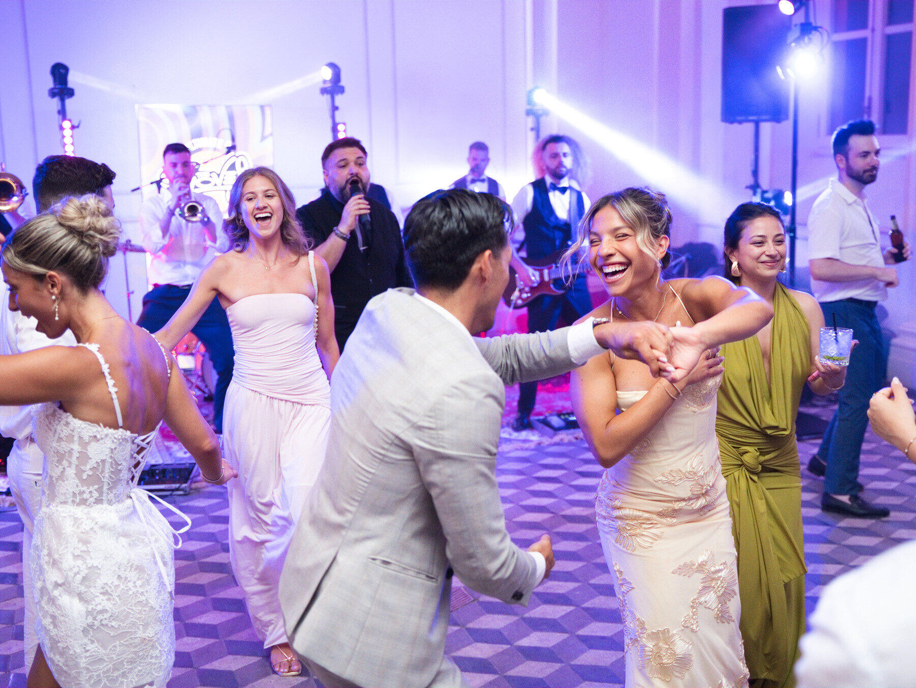 Wedding guests dancing together in front of The Gloves live band under coloured party lights.