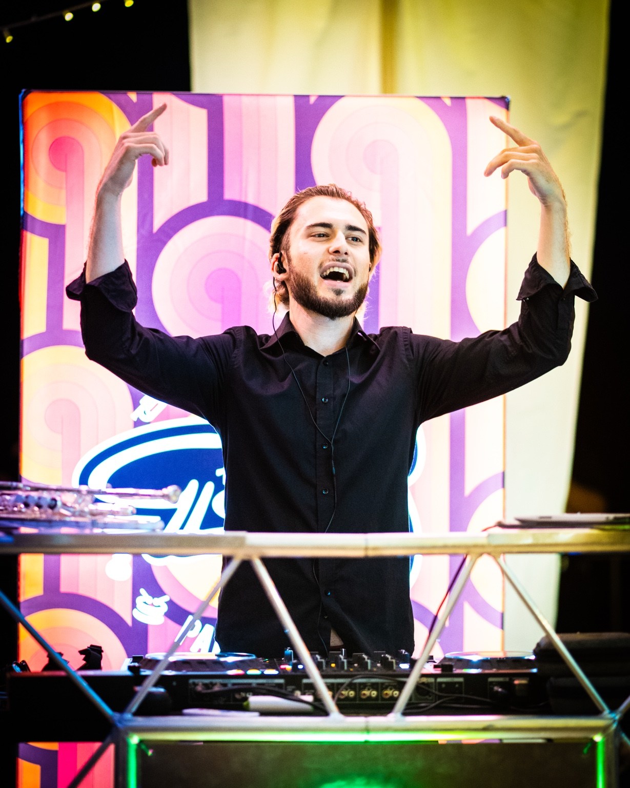 DJ raising both arms behind his console and illuminated backdrop.