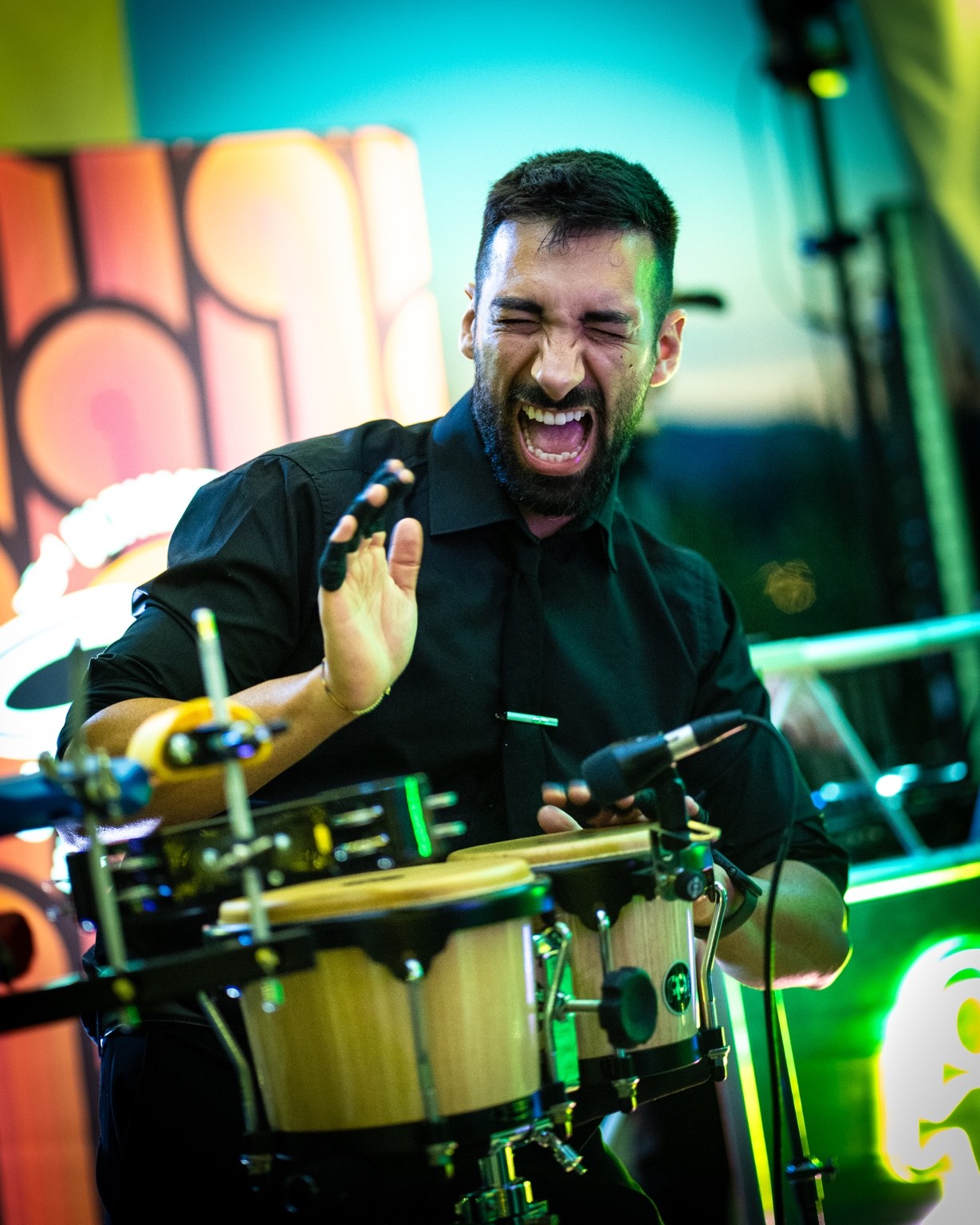Percussionist playing miked bongos under green and blue stage lighting.