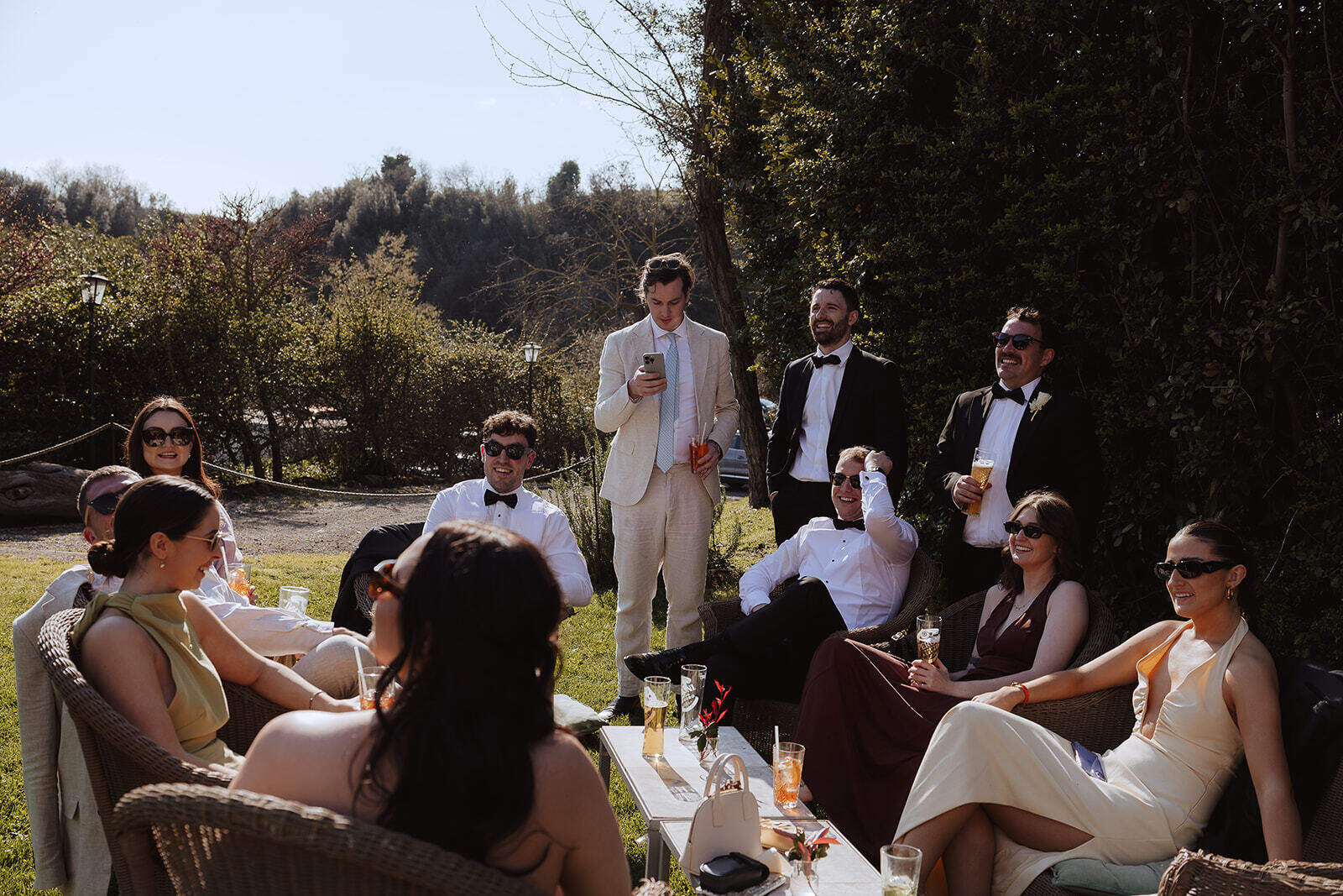 Invitati seduti e in piedi con i bicchieri durante l’aperitivo all’aperto a Borgo di Tragliata.