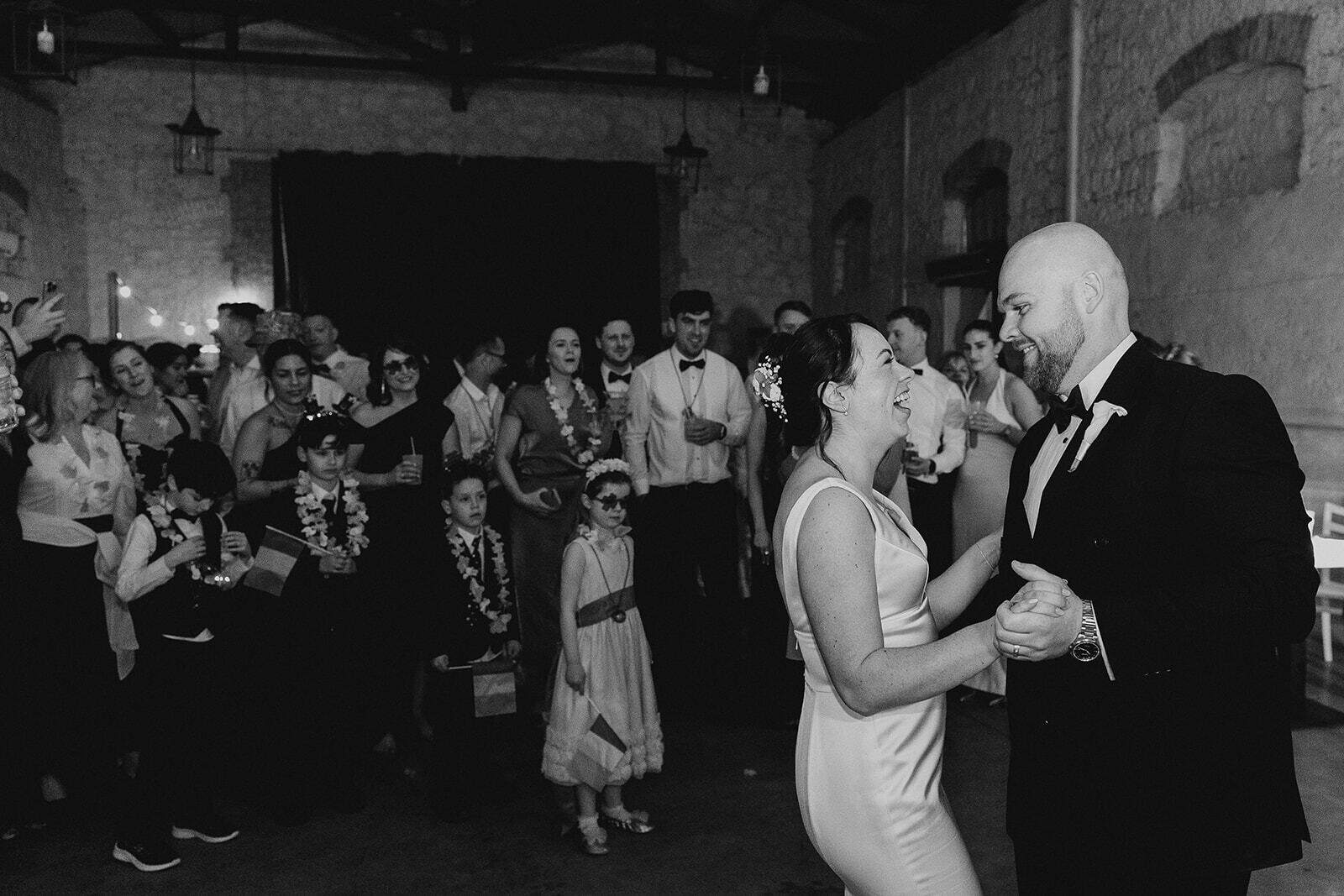 Rebecca e Hugh ballano tenendosi per mano, circondati dagli invitati, in una foto in bianco e nero.